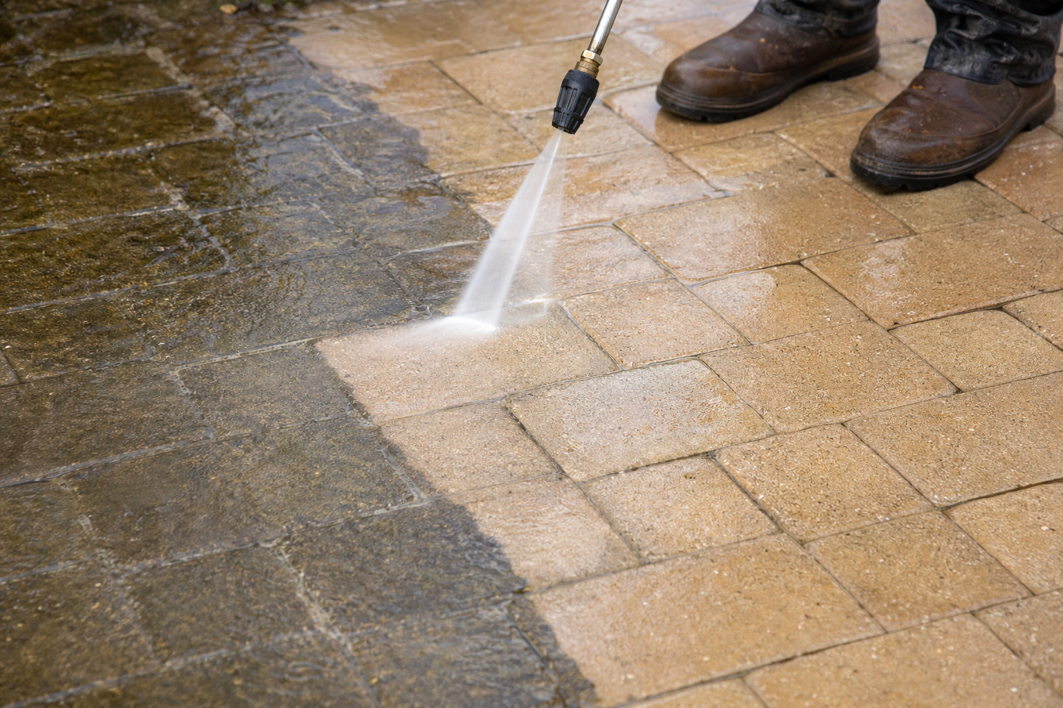 Pressure washing wand cleaning Florida pavers with a visible clean path
